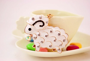 Detailed view of white sheep keychain with sparkling rhinestones on a cream teacup