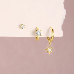 Detail of three gold earrings set with round zircon and an octagonal star charm pendant