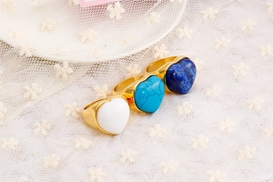 Three heart-shaped gold rings with white, turquoise and blue stones on white lace fabric