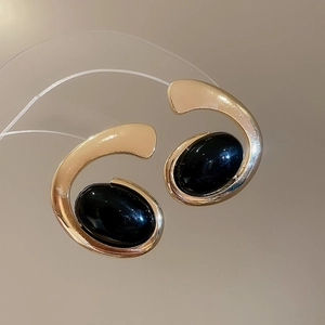 Detailed close-up of C-shaped gold metal earrings featuring large oval black resin gems