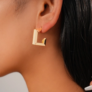 Close-up of a glossy gold geometric U-shaped hoop earring worn on a model's ear