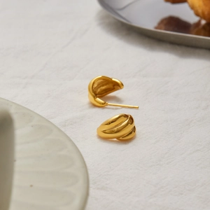 Macro shot of gold-plated hoop earrings with elegant textured folds on white fabric