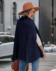 Dettaglio di un poncho in maglia blu scuro a collo alto con vestibilità ampia e trama