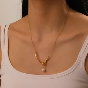 Golden V-shaped knot pendant necklace with white pearl on a fashion model neckline