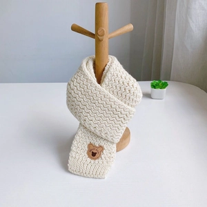Detail view of beige knitted scarf with thick wave texture and brown bear patch