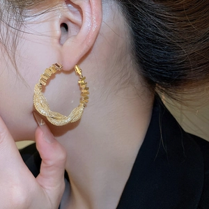 Close-up of a model wearing large golden twisted hoop earrings with a textured surface