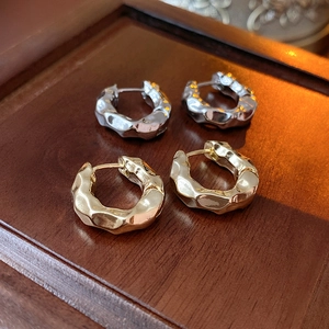 Detail of gold and silver hoop earrings with a hammered metal texture on wood
