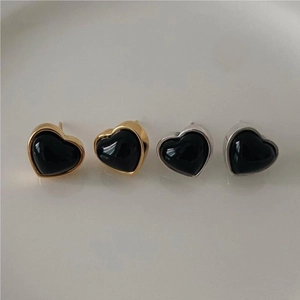 Detail of gold and silver heart-shaped black onyx earrings on a ceramic dish