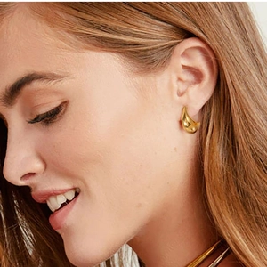 Close-up of golden C-shaped hollow earrings worn by a model to show elegant design
