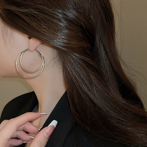 Detail view of double hoop silver-tone layered earrings on model showing textured metal design
