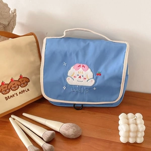 Close-up of blue nylon cosmetic bag with embroidery, handle, and hanging hook detail