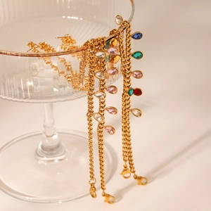 Detailed view of gold Cuban link bracelets with colorful teardrop zircon charms on glass decor