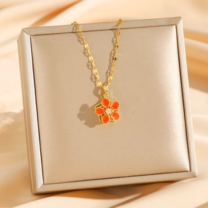 Elegant gold titanium steel necklace with orange rotating flower pendant on silk display