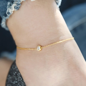 Gros plan d'une chaîne de cheville en acier titane doré avec un diamant rond brillant
