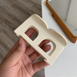 Detailed close-up of cream-colored acetate hair claw clip in a stylish geometric B-letter shape