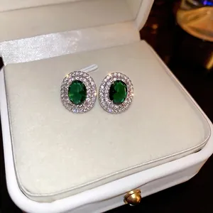 Elegant emerald-green oval stud earrings with double halo diamonds in a jewelry box