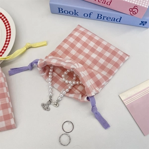 Pink checkered drawstring pouch with a pearl necklace and silver minimalist rings