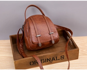 Close-up of vintage brown leather bag with dual metal zippers and textured finish