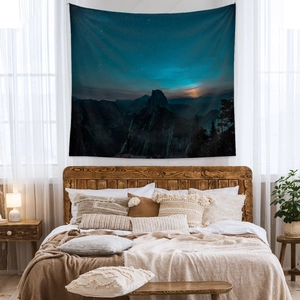 Bohemian starry night sky tapestry with mountains above a cozy bed in a bedroom