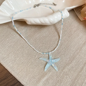 Detail of beaded starfish necklace placed on a seashell against a linen background