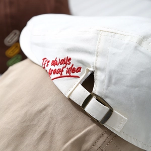 Detail of white cotton cap with red hand-drawn embroidery and metal buckle closure