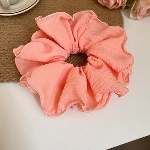 Detailed texture of sakura pink pleated fabric scrunchie on rustic straw mat