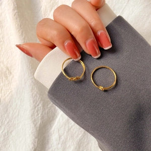 Detailed close-up of two minimalist gold knot rings held against a textured fabric background