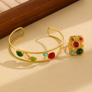Detail of vintage gold-plated jewelry set with colorful cabochon stones on beige surface