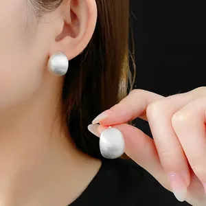 Brushed silver circular stud earrings with minimalist matte finish on black background