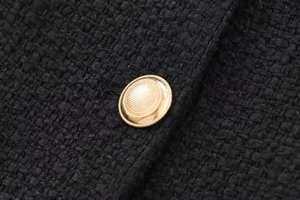 Detailed close-up of a golden textured metal button on premium black woven tweed fabric