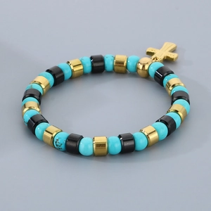 Détail d'un bracelet bohème en perles de turquoise avec breloque croix dorée sur gris