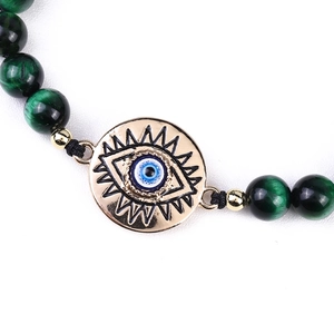 Macro detail of natural green tiger eye beads and golden evil eye charm on the bracelet