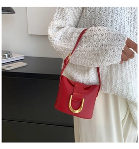 Detail of red leather shoulder bag with gold D-ring buckle worn on a white sweater
