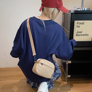 Detail view of a beige canvas crossbody phone bag shown worn by a model in a lifestyle setting