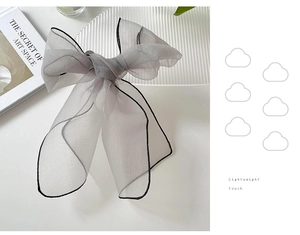 Detail of grey translucent organza hair bow with elegant black piping on soft fabric