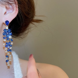 Close-up of elegant flower drop earrings with blue crystals on a female model