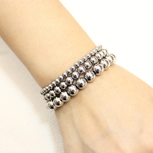 Set of four polished silver stainless steel bead bracelets layered on a model's wrist