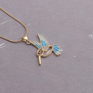 Golden hummingbird pendant necklace with blue enamel wings and crystals on paper background