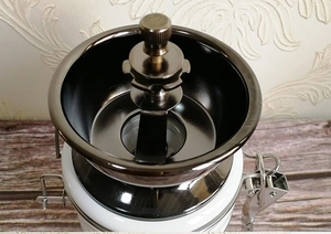 Close-up of manual coffee grinder with dark metal funnel and white ceramic storage jar