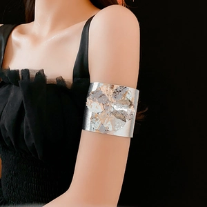 Detail shot of a large silver metal flower cuff bracelet worn on an upper arm over black dress