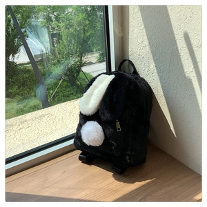 Close-up of black fuzzy bunny backpack with long ears on a wooden ledge in sunlight