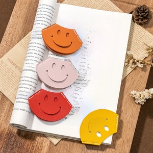Minimalist leather smiley bookmarks in four colors placed on an open book page