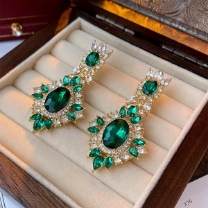 Macro detail of emerald-green oval earrings with sparkling crystals in a wooden box