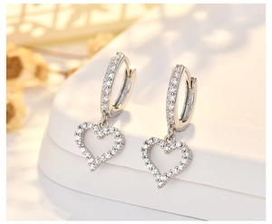 Macro shot of silver heart drop earrings with white zircons on a white display stand
