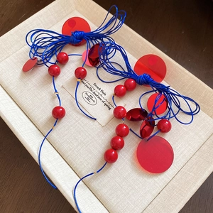 Close-up of red acrylic resin discs and dark blue knotted cords with gold metal rings