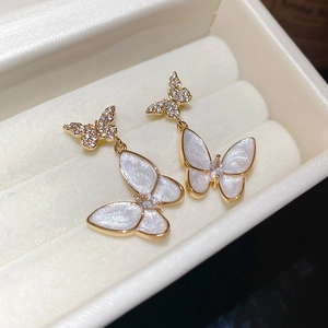 Close-up of golden butterfly earrings with sparkling zircons on white velvet box