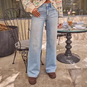 Lichtblauwe jeans met hoge taille en wijde pijpen gedragen door model op een terrasje