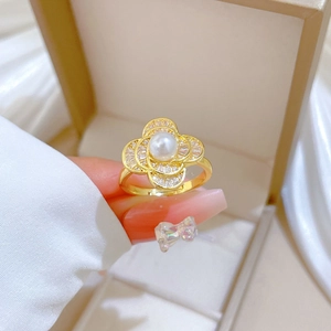 Close-up of a golden pearl ring with pavé diamonds held over a beige jewelry box