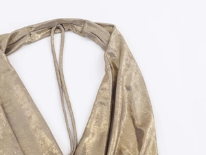 Close-up of gold metallic halter neck detail and shimmering textured fabric on the dress