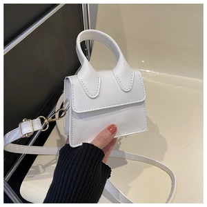 Nahaufnahme einer weißen Mini-Handtasche mit goldenen Schnallen und abnehmbarem Gurt